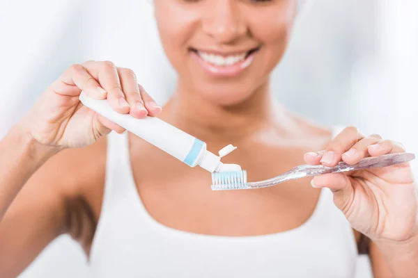 Enfoque selectivo de la mujer joven poniendo pasta de dientes en el cepillo de dientes - foto de stock