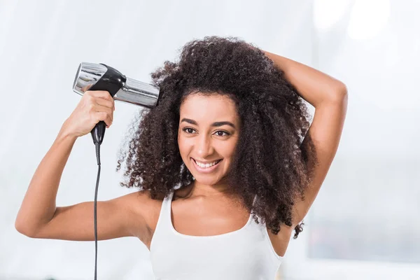 Sonriente rizado africano americano chica secar cabello en casa - foto de stock