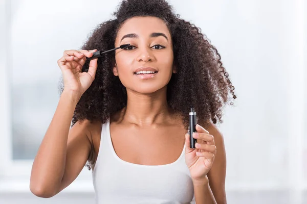 Encaracolado menina americana africana usando rímel e olhando para a câmera — Fotografia de Stock