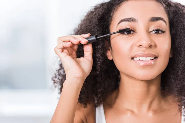 Close up view of curly african american girl using mascara and looking at camera — Stock Photo