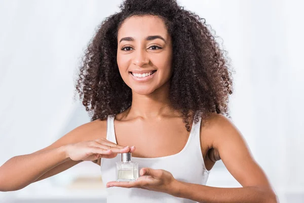 Laughing young woman with curly hair holding perfume bottle — Stock Photo