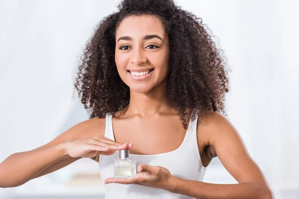 Risueño joven mujer con pelo rizado celebración perfume botella - foto de stock