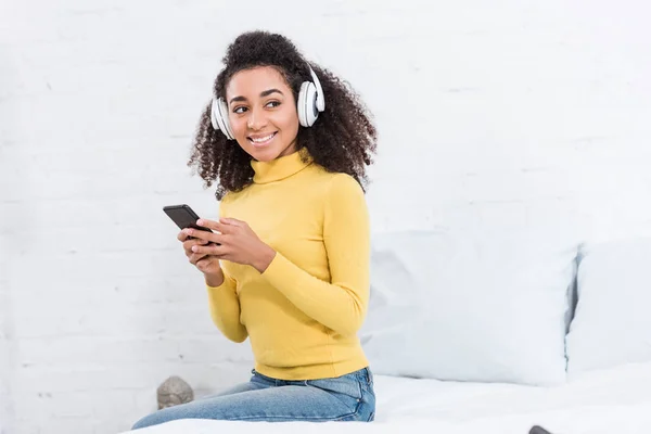 Mujer afroamericana en auriculares escuchando música con smartphone en casa - foto de stock