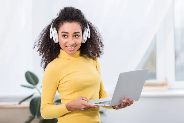 Afro-américaine femme pigiste dans les écouteurs travaillant sur ordinateur portable au bureau à la maison — Photo de stock