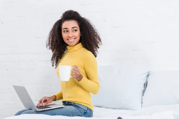 Curly african american female freelancer with coffee cup working on laptop at home — Stock Photo