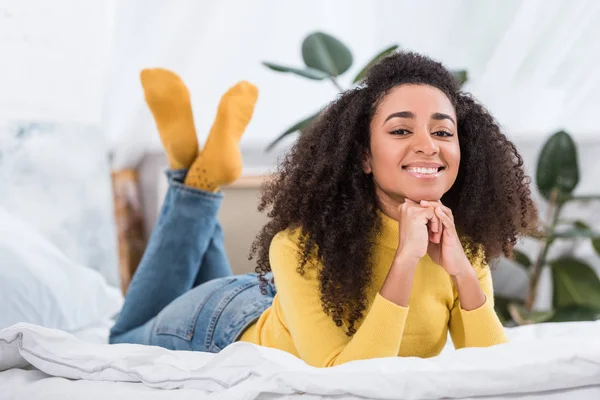 Позитивна афроамериканська молода жінка лежить у ліжку і дивиться на камеру — стокове фото