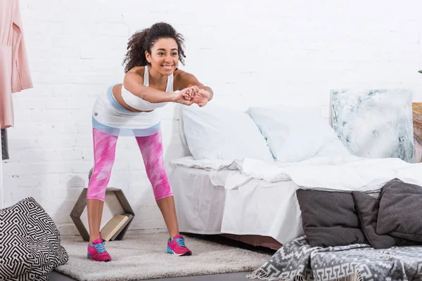 Cheerful african american woman doing exercise during morning time in bedroom at home — Stock Photo