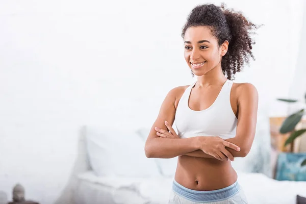 Selective focus of young african american curly girl with crossed arms in bedroom at home — Stock Photo