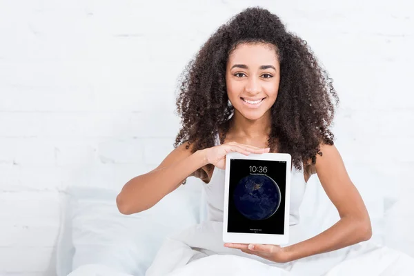 Menina americana africana feliz mostrando ipad tablet na cama em casa — Fotografia de Stock