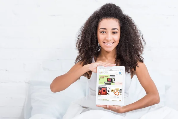 Menina americana africana feliz mostrando tablet digital com ebay na tela na cama em casa — Fotografia de Stock