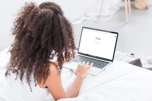 Rear view of curly woman using laptop with google on screen in bed at home — Stock Photo