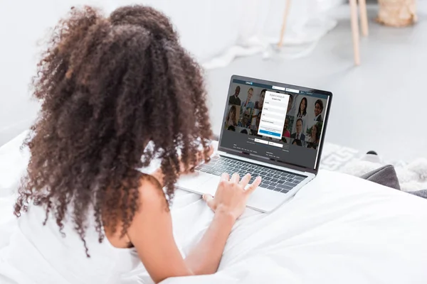 Rear view of curly woman using laptop with linkedin on screen in bed at home — Stock Photo