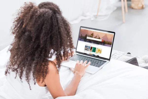 Rear view of curly woman using laptop with shutterstock on screen in bed at home — Stock Photo