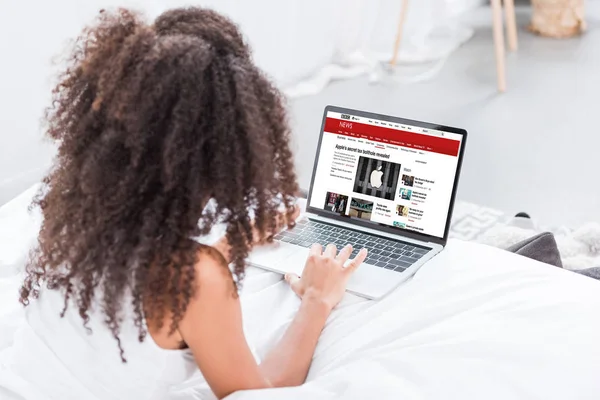 Rear view of curly woman using laptop with bbc news on screen in bed at home — Stock Photo