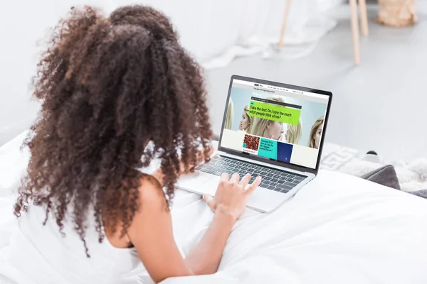 Rear view of curly woman using laptop with bbc science on screen in bed at home — Stock Photo