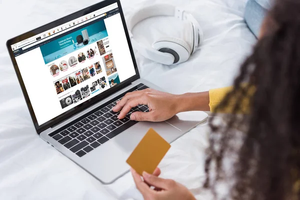 Cropped image of woman holding credit card and using laptop with amazon  on screen — Stock Photo