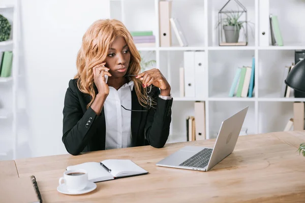 Pensive african american businesswoman talking on smartphone in office — Stock Photo