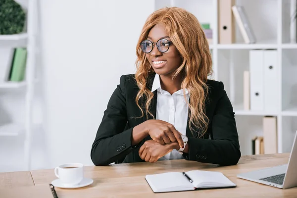 African american businesswoman sitting in glasses with cup and notebook in office — Stock Photo