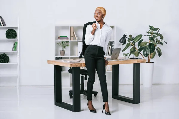 Feliz africana americana mujer de negocios con pelo corto celebración chaqueta en la oficina moderna - foto de stock