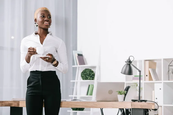 Mulher de negócios americana africana alegre com copo de cabelo curto segurando com bebida no escritório moderno — Fotografia de Stock