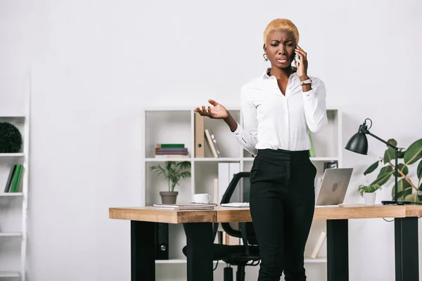 Bouleversé afro-américaine femme d'affaires avec les cheveux courts parler sur smartphone dans le bureau moderne — Photo de stock