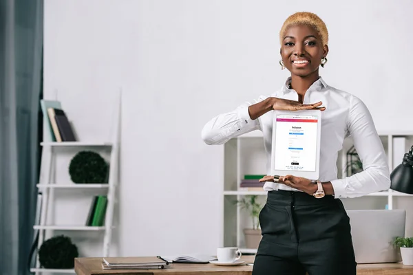 Cheerful african american woman showing digital tablet with instagram app on screen — Stock Photo