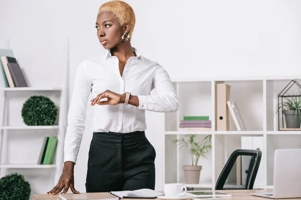 Serious african american businesswoman with short hair standing near table in modern office — Stock Photo