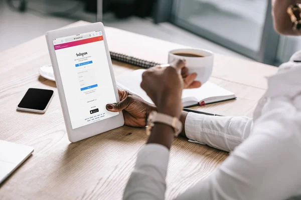 Vue recadrée de femme afro-américaine tenant tablette numérique avec application instagram et tasse de café — Photo de stock