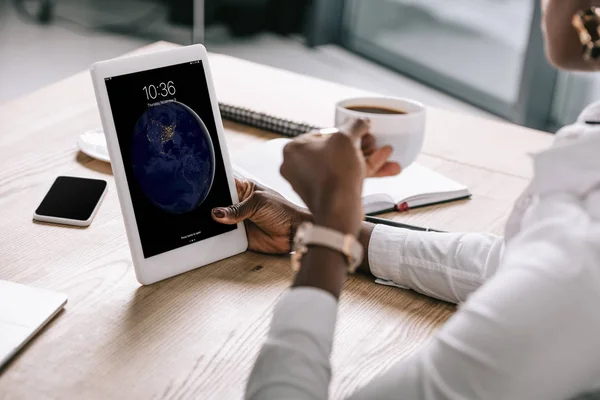 Ausgeschnittene Ansicht einer afrikanisch-amerikanischen Frau mit Tasse und digitalem Tablet mit Sperrbildschirm — Stockfoto