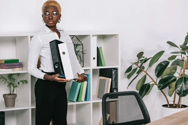 Beautiful african american businesswoman holding folders in modern office — Stock Photo