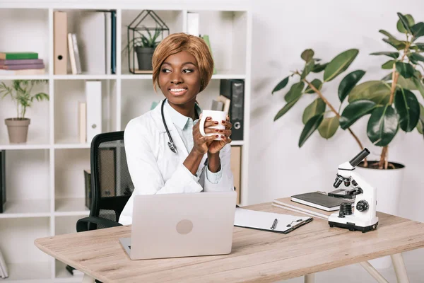 Sorridente scienziata afro-americana in possesso di tazza con bevanda — Foto stock
