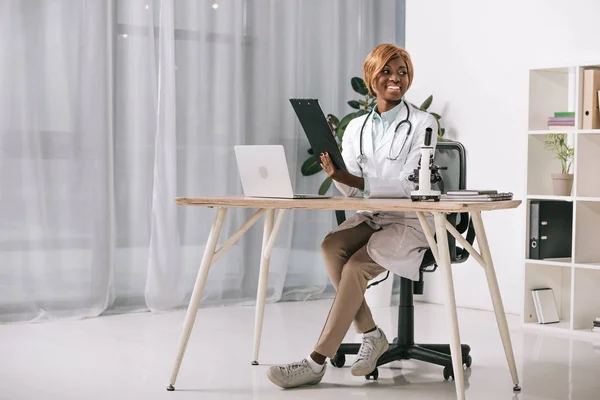Attraente scienziato africano americano seduto con stetoscopio e tenendo appunti — Foto stock