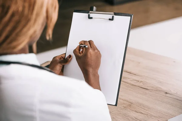 Vista recortada del científico afroamericano escribiendo sobre papel - foto de stock