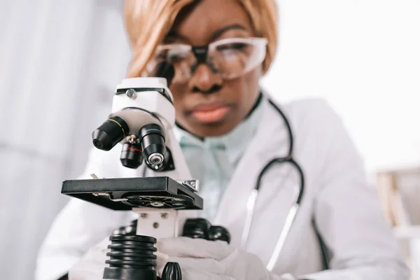 Selective focus of microscope with female african american scientist on background — Stock Photo