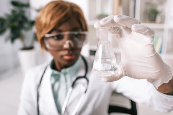 Selective focus of glass test tube with liquid in hand of female african american scientist — Stock Photo