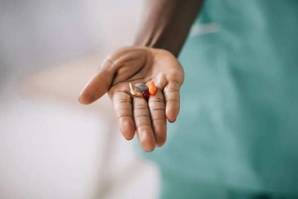 Vue recadrée de femme afro-américaine tenant des pilules dans la main — Photo de stock