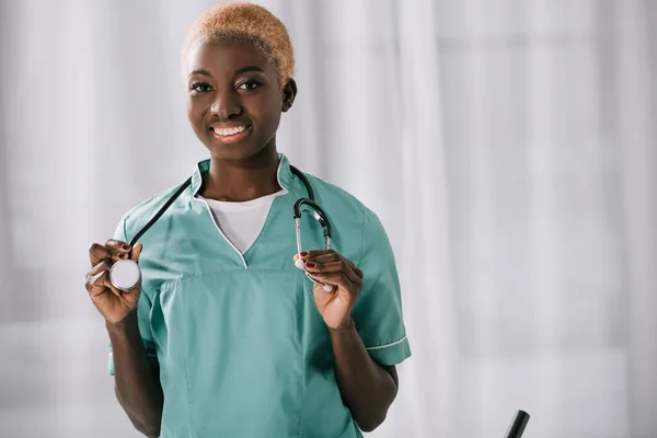 Attraente donna afro-americana allegra che tiene lo stetoscopio mentre guarda la fotocamera — Foto stock