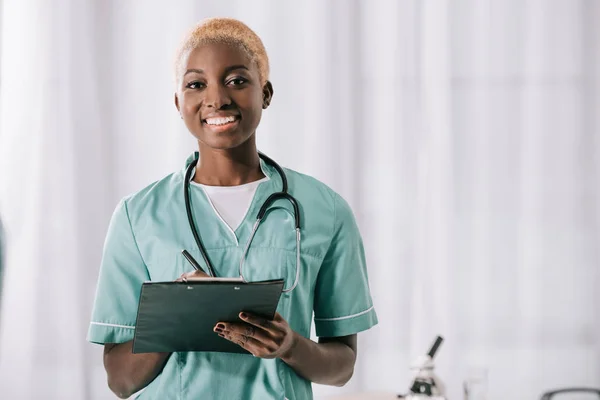 Smiling african american woman with stethoscope and clipboard — Stock Photo