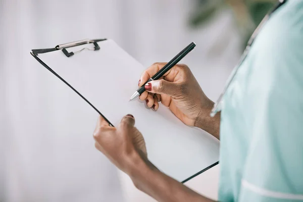 Cropped view of african american nurse writing in clipboard with paper — Stock Photo