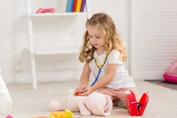 Adorable child examining soft rabbit toy with stethoscope in children room — Stock Photo
