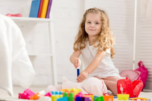 Criança adorável examinando brinquedo de coelho com na sala de crianças e olhando para a câmera — Fotografia de Stock