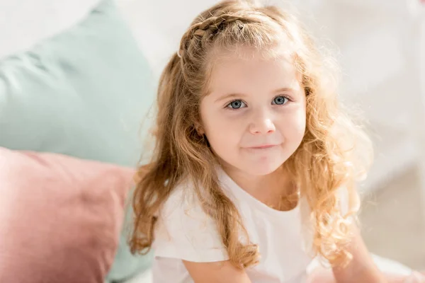 Aus der Vogelperspektive: entzückendes Kind mit lockigem Haar, das im Kinderzimmer in die Kamera schaut — Stockfoto