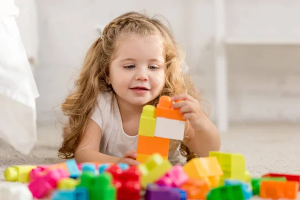 Selective focus of adorable kid playing with colored plastic constructor on carpet in children room — Stock Photo