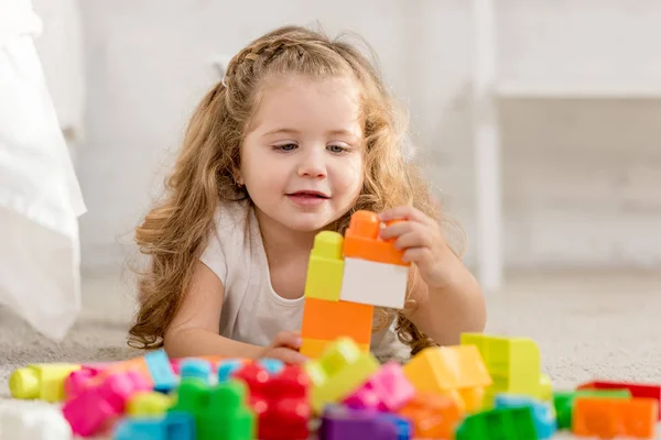 Enfoque selectivo de adorable niño jugando con el constructor de plástico de color en la alfombra en la habitación de los niños - foto de stock