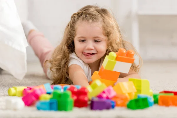 Niño adorable feliz jugando con el constructor plástico de color en la alfombra en la habitación de los niños - foto de stock