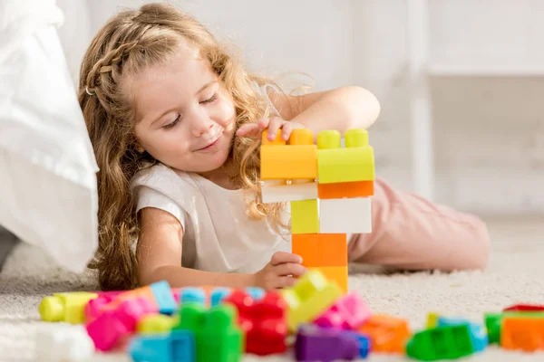 Adorable niño jugando con el constructor plástico de color en la alfombra en la habitación de los niños - foto de stock