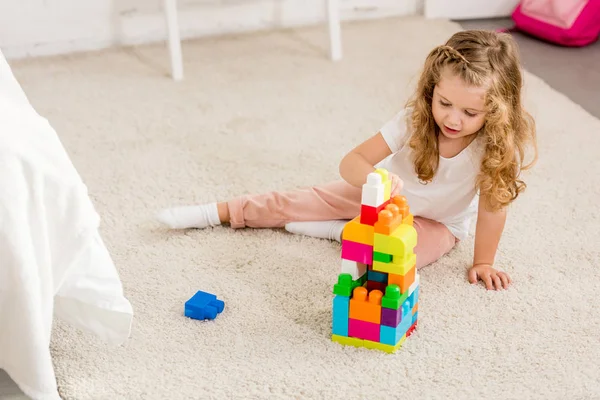 Vista ad alto angolo di adorabile bambino che gioca con il costruttore di plastica colorata sul tappeto nella stanza dei bambini — Foto stock