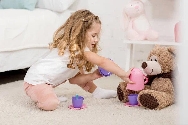 Чарівна дитина грає з плюшевим ведмедем на підлозі в дитячій кімнаті — стокове фото