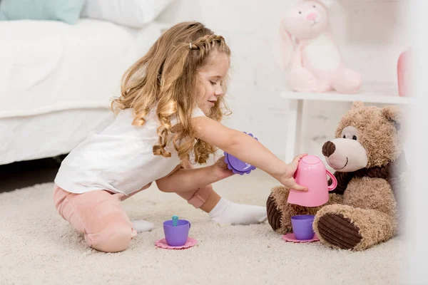 Adorable niño jugando con osito de peluche en el suelo en la habitación de los niños - foto de stock