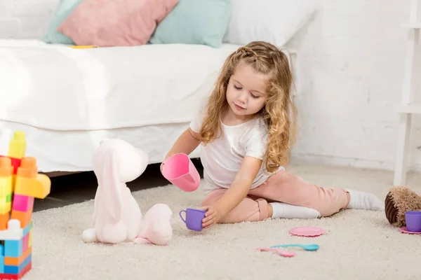 Adorabile bambino che gioca con il giocattolo del coniglio e bicchieri di plastica nella stanza dei bambini — Foto stock